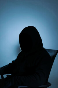 a silhouette of a man with a hoodie sitting. a portrait of an unidentified person suitable for a campaign, advertisement, poster, etc. related to scamming, phishing, and other internet threats.