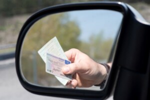 In einem Seitenspiegel eines Autos ist zu erkennen, dass eine Person den Fahrzeugschein und den Führerschein aus dem Fenster reicht.